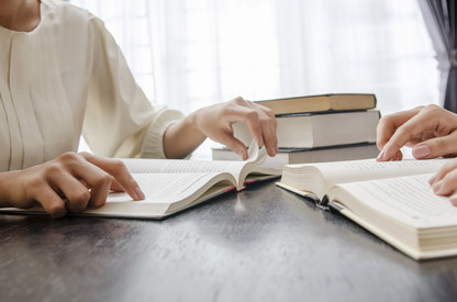 Zwei Personen sitzen mit Büchern an einem Tisch und lesen.