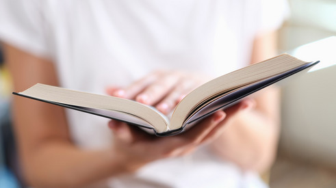 Person hält ein Buch in den Händen und liest.